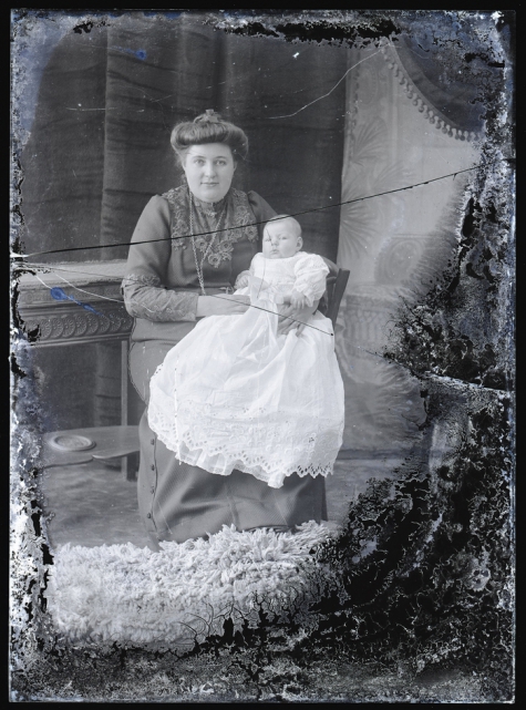 Zittend portret, jonge vrouw met opgestoken haar, halsketting, met baby op de schoot, Melle, 1910-1920