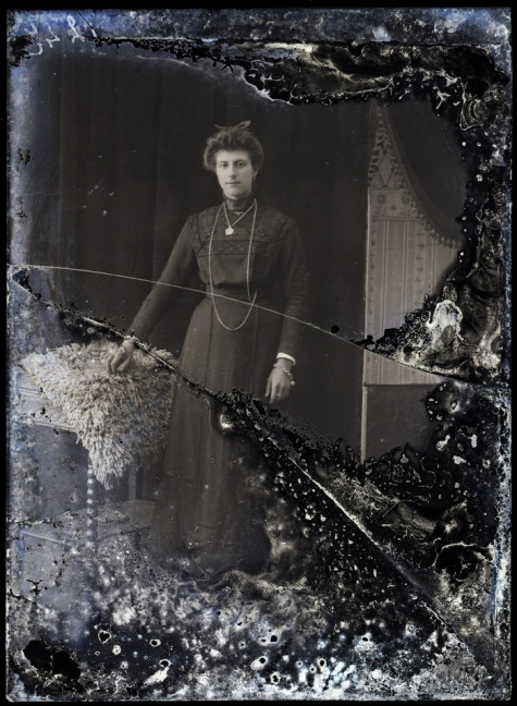    Staand portret van jonge vrouw in feestkledij, opgestoken haar met strik, halsketting en armband, Melle , 1910-1920