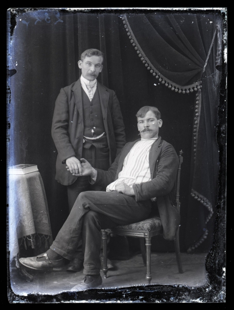 Portret van staande man in feestkledij met wit hemd en stropdas en zittende man, beiden met snor en kuifvormig gekamd haar , Melle , 1910-1920
