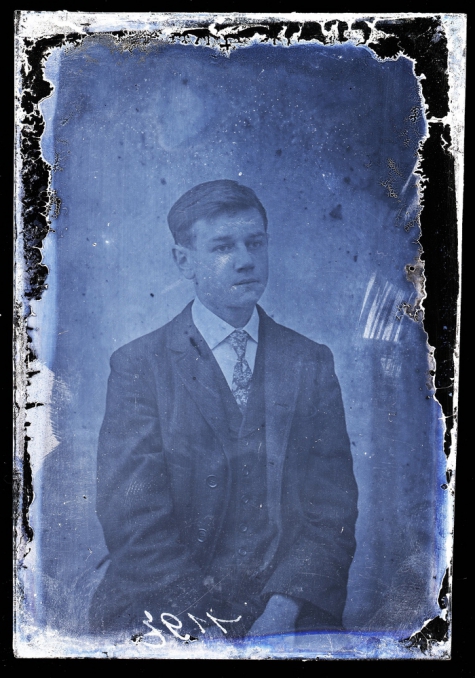 Zittend portret van jonge man in feestkledij bestaande uit kostuum en wit hemd met stropdas, kuifvormig opzij gekamd   haar, Melle , 1910-1920