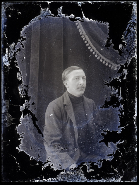 Zittend portret man van middelbare leeftijd met vest en gestreepte pullover met hoge kraag, strak opzijgekamd haar, Melle , 1910-1920