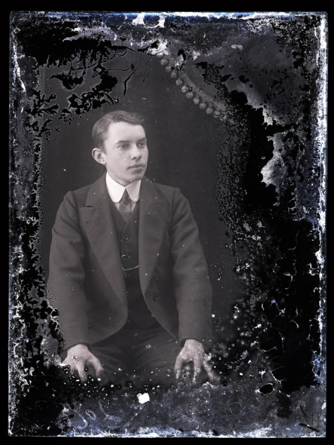 Zittend portret van jonge man in feestkledij met kostuum en witte hemdskraag met stropdas, golvend kuifvormig gekamd haar, Melle, 1910-1920