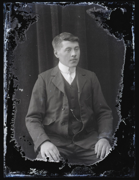 Zittend portret van jonge man in feestkledij bestaande uit kostuum met wit hemd en fijne stropdas, golvend haar zijwaarts naar links gekamd, Melle, 1910-1920