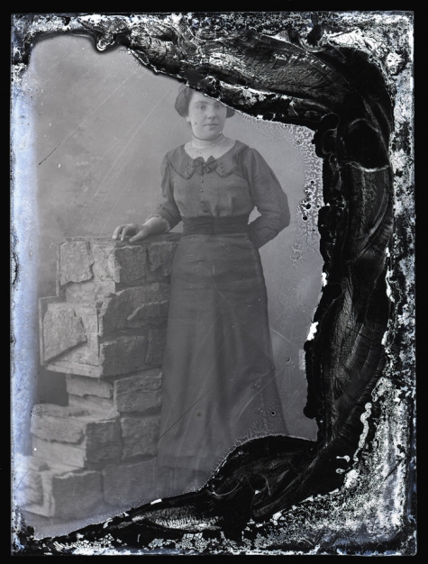 Staand portret van jonge vrouw in feestkledij bestaande uit lang kleed met brede heupband en driekwart mouwen, opgestoken haar, Melle, 1910-1920