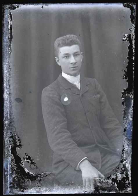 Zittend portret van jonge man in feestkledij bestaande uit kostuum, wit hemd en stropdas, kuifvormig naar achter gekamd haar, Melle, 1910-1920