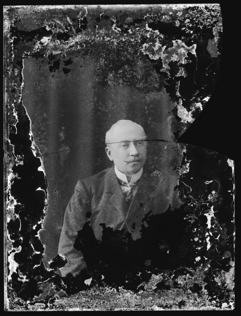 Zittend portret van man in feestkledij bestaande uit kostuum en wit hemd met stropdas, gemodelleerde snor, Melle, 1910-1920