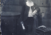 Rechtstaande foto van jongeman in feestkledij met wit hemd en witte kraag, kortgeknipt haar, opgerold document in rechterhand, Melle , 1910-1920
