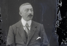 Zittend portret van man in kostuum en wit hemd met stropdas, gemodelleerde snor en strak gekamd haar, Melle , 1910-1920