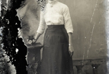 Staand portret van jonge vrouw in feestkledij bestaande uit lange rok en witte bloes met driekwart mouwen, opgestoken haar, Melle , 1910-1920
