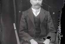 Zittend portret van man in feestkledij met kostuum en witte opstaande hemdskraag met stropdas, gemodelleerde snor en hoofdhaar met middenscheiding, Melle, 1910-1920