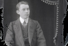Zittend portret van jonge man in feestkledij met kostuum en witte hemdskraag met stropdas, kuifvormig naar links gekamd haar, Melle, 1910-1920