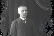 Zittend portret van man in feestkledij met wit hemd en stropdas, gemodelleerde snor en glad naar rechts gekamd haar, Melle, 1910-1920