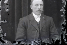 Zittend portret van man in feestkledij met witte hemdsboord en stropdas, gemodelleerde snor en en strak naar rechts gekamd haar, Melle, 1910-1920