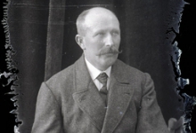 Zittend portret van man in feestkledij met witte hemdsboord en donkere stropdas, gemodelleerde snor en kalend voorhoofd, Melle, 1910-1920