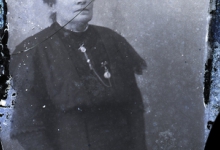 Zittend portret vrouw in donkere feestkledij, opgemaakt haar en borstketting, Melle, 1910-1920