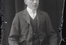 Zittend portret van jonge man in feestkledij bestaande uit kostuum met wit hemd en fijne stropdas, golvend haar zijwaarts naar links gekamd, Melle, 1910-1920