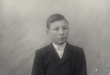 Zittend portret van jongen in feestkledij bestaande uit kostuum met wit hemd en stropdas, plat naar rechts gekamd haar, Melle, 1910-1920