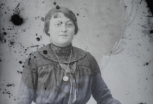 Staand portret van jonge vrouw in feestkledij bestaande uit lange rok en bloes met lange mouwen, stropdas en halsketting, bolvormig gekamd haar, Melle, 1910-1920